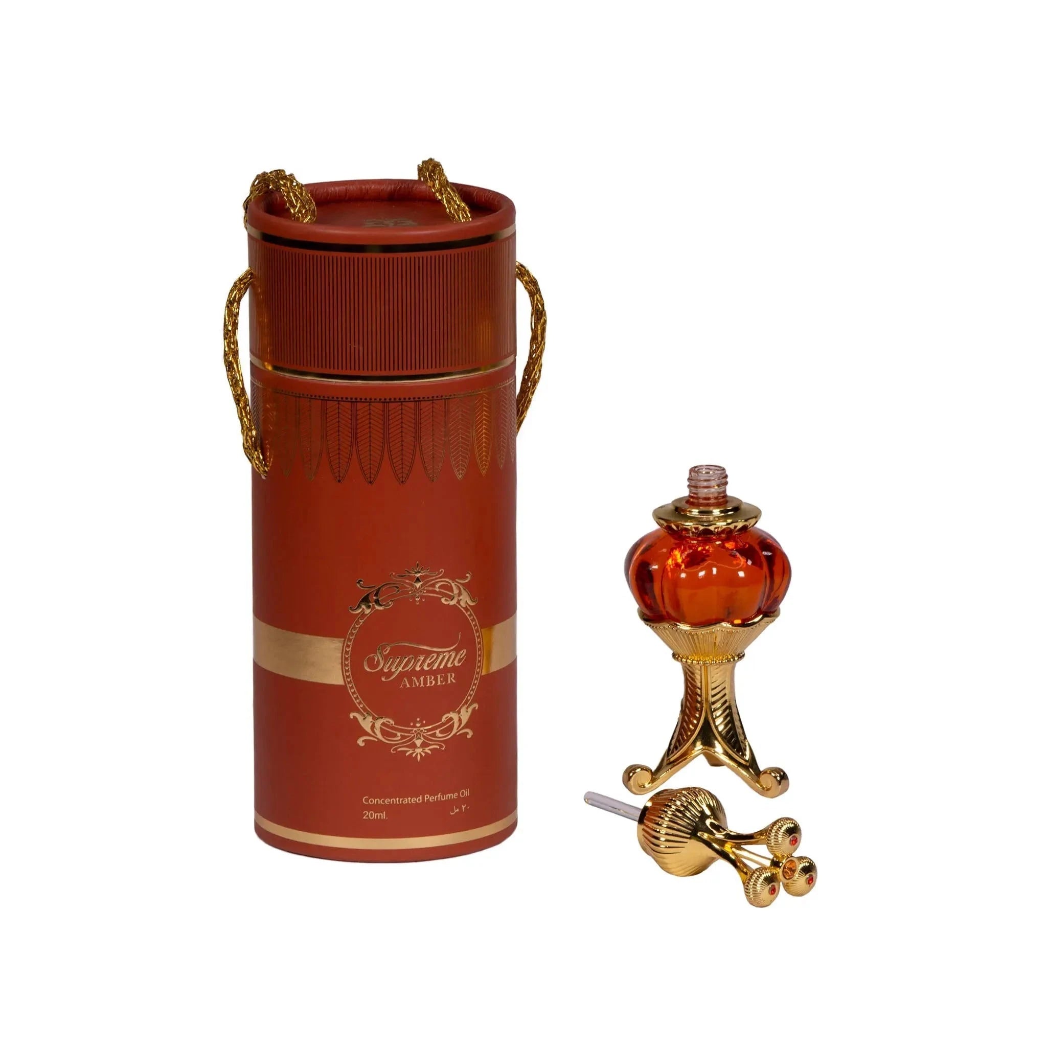The image depicts a luxurious perfume oil set featuring a red cylindrical container with gold accents and a red and gold perfume oil bottle resting on an ornate golden stand. The container, adorned with a golden motif and the words "Supreme AMBER Concentrated Perfume Oil 20ml", has a lid with elegant gold rope handles. Beside it, the spherical bottle has a rich, amber color with a gold-detailed cap, and its gold applicator rod is placed in front of the stand.