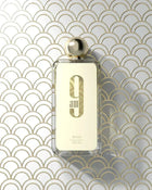 The image displays a transparent perfume bottle with a golden cap, set against a geometric patterned background composed of overlapping arches in gold and white.  Below this is the brand name "AFNAN" in smaller, capitalized letters. The product specifications "eau de parfum vaporisateur," "100ml," and "3.4fl.oz" are listed at the bottom of the label. The overall aesthetic is luxurious and modern.
