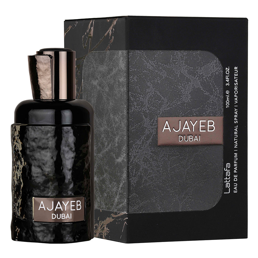 A sleek black and gray box of "Ajayeb Dubai" Eau de Parfum by Lattafa, featuring a textured design and the product name in white and bronze text on the front. The box is placed next to a matching perfume bottle with a glossy, hammered black finish.