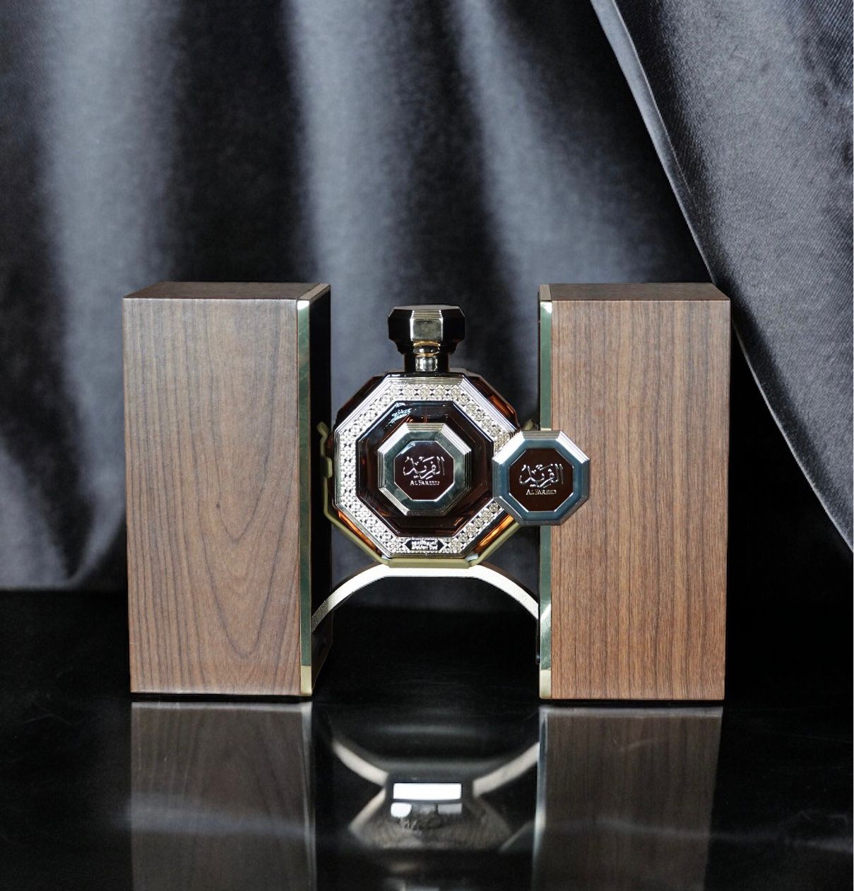 A sophisticated perfume display featuring an ornate octagonal bottle with a black body and silver detailing, accompanied by two wooden textured panels with metallic edges. The panels and the bottle all bear the "Al Fareed" logo in Arabic script, indicative of a luxurious Arabian oud fragrance. The setup is presented against a dark, draped background, reflecting an opulent and elegant ambiance.