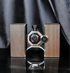 A sophisticated perfume display featuring an ornate octagonal bottle with a black body and silver detailing, accompanied by two wooden textured panels with metallic edges. The panels and the bottle all bear the "Al Fareed" logo in Arabic script, indicative of a luxurious Arabian oud fragrance. The setup is presented against a dark, draped background, reflecting an opulent and elegant ambiance.