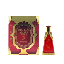A red-and-gold rectangular box labeled 'Amber Pure' stands beside a matching red glass perfume bottle with ornate gold accents and 'Khadlaj' branding.