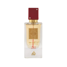 Image of a rectangular clear glass perfume bottle with a red cap embellished with two crystals. The bottle features a gold label with intricate arabesque designs and Arabic calligraphy that reads '??? ????' (Ana Abiyedh), with 'ROUGE' printed in red below. Below the gold label is the brand logo in gold with a flame-like design and the word 'Lattafa'. The perfume liquid appears to be a pale amber color, and the overall design suggests luxury and exotic allure.