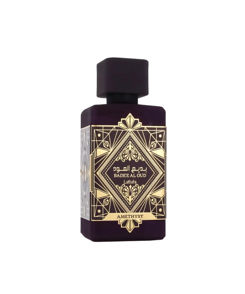 The image features a sophisticated perfume bottle of "Bade'e Al Oud Amethyst" by Lattafa. The bottle has a solid, dark purple hue that exudes luxury and depth. It's square in shape with a flat, wide body and a modest, dark purple cap. The front of the bottle is adorned with intricate golden geometric patterns and Arabic calligraphy, emphasizing the brand's rich cultural heritage.