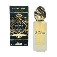 The image features a frosted glass perfume bottle with a golden ribbed cap and a black and gold packaging box. The box has an intricate geometric and arabesque design in black and gold, with the name "OUD FOR GLORY" and "BADEE AL OUD" prominently displayed, alongside the brand "Lattafa." The box also specifies "50ML / FRESH HAIR MIST / 1.7 FL.OZ." 