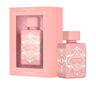 A pink rectangular box with a transparent window, labeled ‘Badee Al Oud Noble Blush’ by Lattafa, displayed next to a matching pink perfume bottle adorned with intricate white geometric patterns and a square cap