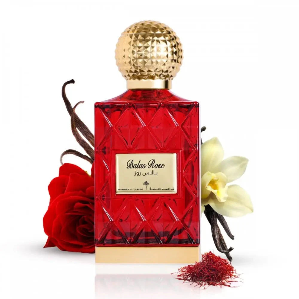 The image depicts a red glass perfume bottle with a golden, textured cap, labeled "Balas Rose" in English with Arabic script above it, suggesting the fragrance's name by the brand Ibraheem Al Qurashi.   In the composition, there's a red rose to the left, suggesting the scent's floral nature, vanilla beans to the left, indicating a warm, sweet note, a white flower (possibly vanilla or orchid) to the right, and a small pile of red saffron threads in the front right, hinting at the luxurious ingredients.