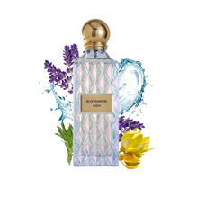 The image shows a clear, faceted glass perfume bottle with a gold cap and a label that reads "BLUE DIAMOND AQUA." The bottle is surrounded by visual elements that evoke the scent's character: sprigs of purple lavender on the left, splashing water droplets around the bottle, and yellow ylang-ylang flowers on the right. The overall presentation suggests a fresh, aquatic, and floral fragrance, with a luxurious and clean aesthetic emphasized by the white background.