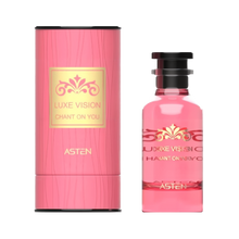 A pink, cylindrical perfume box with a gold-accented Luxe Vision Chant On You label beside a matching pink glass perfume bottle adorned with a decorative gold motif