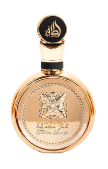 Image of a round, gold-colored perfume bottle with a large circular cap. The cap features black Arabic calligraphy and the brand name 'Lattafa' in English. The bottle has a decorative, embossed flower design in the center with elegant braided detailing along the edges and the inscription 'Fakhar Lattafa' below it. The overall design conveys luxury and traditional aesthetics, with a focus on reflective gold surfaces and contrasting black details.
