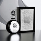 An image of a black and silver perfume bottle alongside its packaging. The bottle features a reflective black surface with a silver flower emblem and a silver cap with Arabic calligraphy. The box is a monochrome grey with elegant arabesque designs and the name "Fakhar Lattafa" in the center, along with "PRIDE OF LATTAFA" below it.
