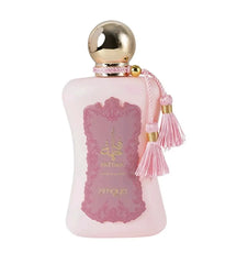 The image shows a bottle of "Fatima" extrait de parfum by Zimaya. The perfume bottle is an elegant, soft pink color with a gold spherical cap. It features a pink label with ornate detailing and gold text, reading "Fatima" in both English and Arabic, along with "extrait de parfum" and the brand name "zimaya" at the bottom. The bottle is adorned with two pink tassels hanging from the neck, adding a touch of luxury and sophistication.