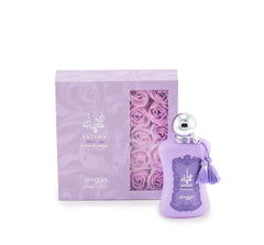 The image shows a bottle of "Fatima Velvet Love" extrait de parfum by Zimaya alongside its packaging. The perfume bottle is a soft lavender color with a silver spherical cap and is adorned with matching lavender tassels.   The accompanying box is also lavender with silver text and a clear window showcasing lavender rose petals inside, enhancing the luxurious and feminine presentation of the product.