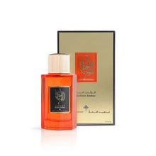 This image features a rectangular, transparent orange bottle of "Golden Amber" perfume by Ibraheem Al Qurashi with a white cap, in front of its packaging. The packaging is a black box with a gold and orange design, matching the perfume bottle's label, which has black Arabic calligraphy and English text. The presentation against a white background emphasizes the product and its packaging.
