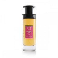 This is an image of a cylindrical clear perfume bottle with a black top and pump. The perfume has a yellow tint and features a pink label with the initials "RT" in large letters, the phrase "HAPPINESS DOSE" in smaller letters, both in English and Arabic, and "ROSE TOBACCO" underneath. The bottle is showcased against a plain white background, focusing on the simplicity and elegance of the design.