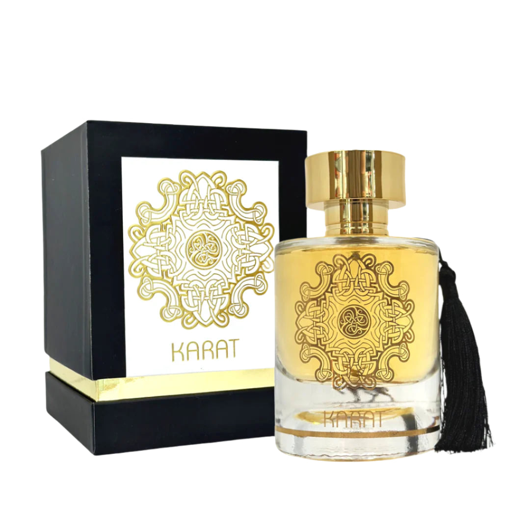 A product image of Lattafa’s “Karat” perfume: a clear cylindrical glass bottle filled with golden liquid, decorated with an intricate gold filigree medallion on its front and topped by a shiny gold cap.