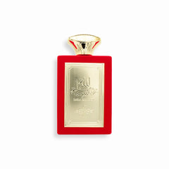 A luxurious bottle of Laila Romancia Eau De Parfum by Sahari, featuring a striking red velvet-textured rectangular design with an elegant gold metallic plate engraved with Arabic calligraphy and the product name. The cap is gold-toned with a flared shape, enhancing the perfume’s sophisticated and regal aesthetic.