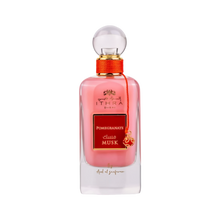A bottle of Ithra Dubai Pomegranate Musk perfume by Ard Al Zaafaran. It features a clear glass design with a white gradient base and a round glass cap. The perfume liquid has a soft pink hue, and there's a gold-colored brand emblem at the top, with the name of the scent on a red and gold label in the center. A small gold charm with intricate detailing is attached to the neck of the bottle with a red string. The presentation suggests a feminine and luxurious fragrance.