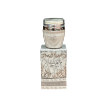 The image shows a product named "Pure Musk Hand and Body Lotion." The lotion is packaged in a light beige container with a clear lid and placed on top of a matching beige box adorned with intricate, elegant silver patterns and Arabic calligraphy. The box prominently features the product name "Pure Musk." The sophisticated packaging suggests a luxurious and high-quality skincare product.