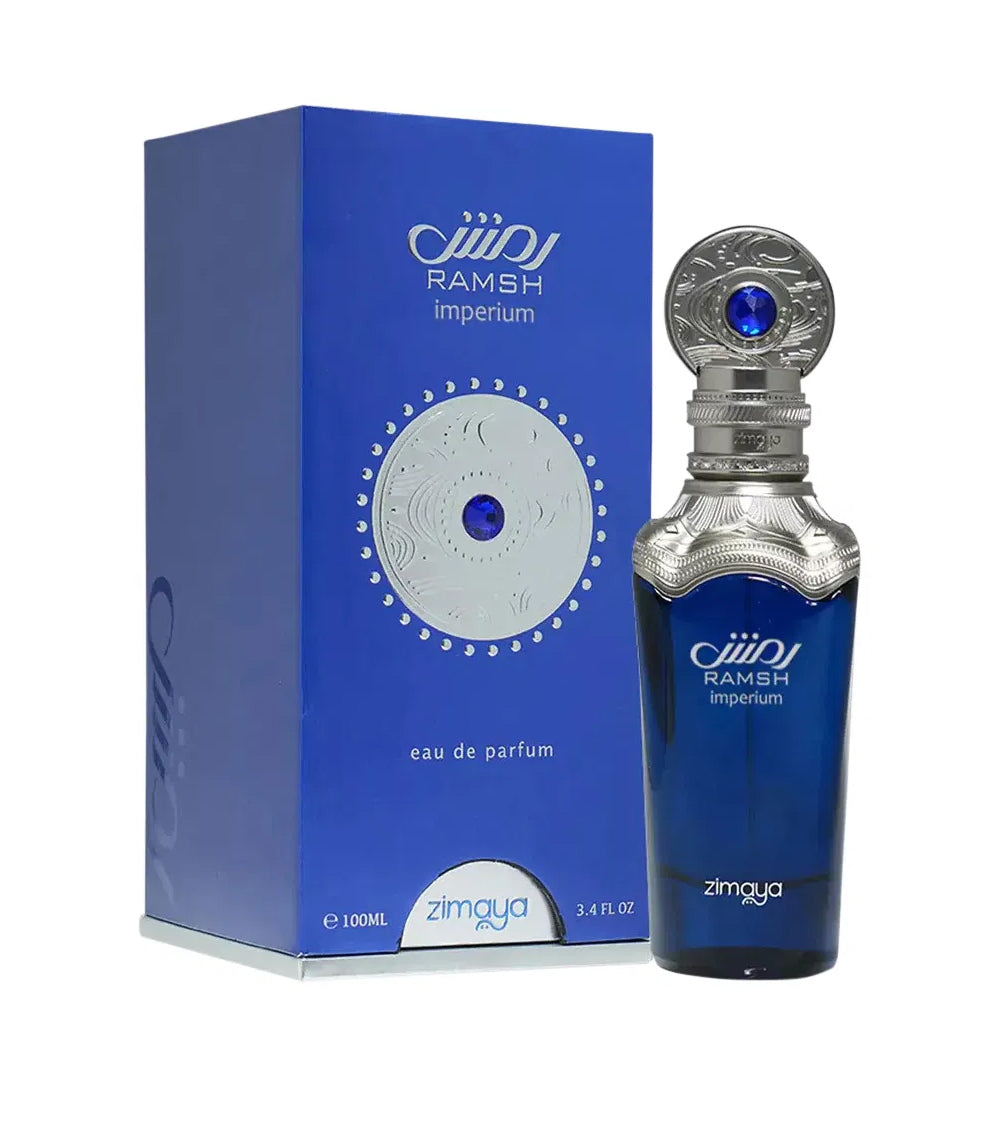 A bottle and packaging of Ramsh Imperium Eau De Parfum by Zimaya. The perfume bottle is a deep blue color with silver metallic detailing at the neck and cap, which features intricate engravings and a prominent blue gemstone-like accent. The label on the bottle reads "RAMSH imperium" along with the Zimaya logo.