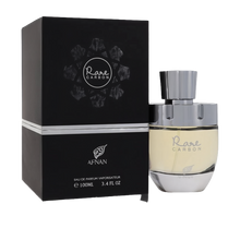 The image features a perfume product called "Rare CARBON" by AFNAN. It shows a sleek perfume bottle alongside its packaging. The bottle has a clear glass bottom where you can see the pale yellow perfume, and a metallic silver cap. The packaging is a square black box with the name "Rare CARBON" encircled by a stylized molecular design in white and grey, suggesting a theme related to carbon or elements. 