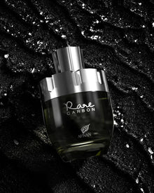 The image depicts a perfume bottle from the brand AFNAN, specifically the "Rare CARBON" fragrance. The bottle has a sleek, modern design with a transparent glass body that fades from clear to a dark gradient at the base, suggesting the color of the perfume within. The bottle is placed against a textured black background with sparkling silver flecks scattered throughout, giving the impression of a luxurious and elegant product. 