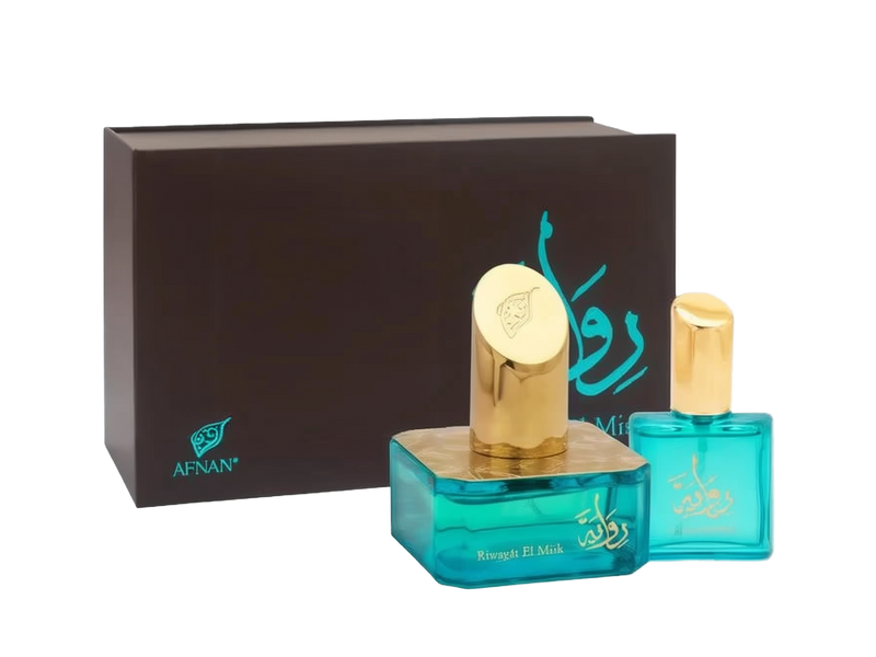 The image presents a pair of perfume bottles against the backdrop of a dark brown box with the brand's logo "AFNAN" in a teal color at the lower left corner. The box features a calligraphic design in teal, likely the perfume's name in Arabic script. The larger perfume bottle has a square base made of translucent teal glass, with a thick gold band around its neck and a round golden cap embossed with a floral emblem.