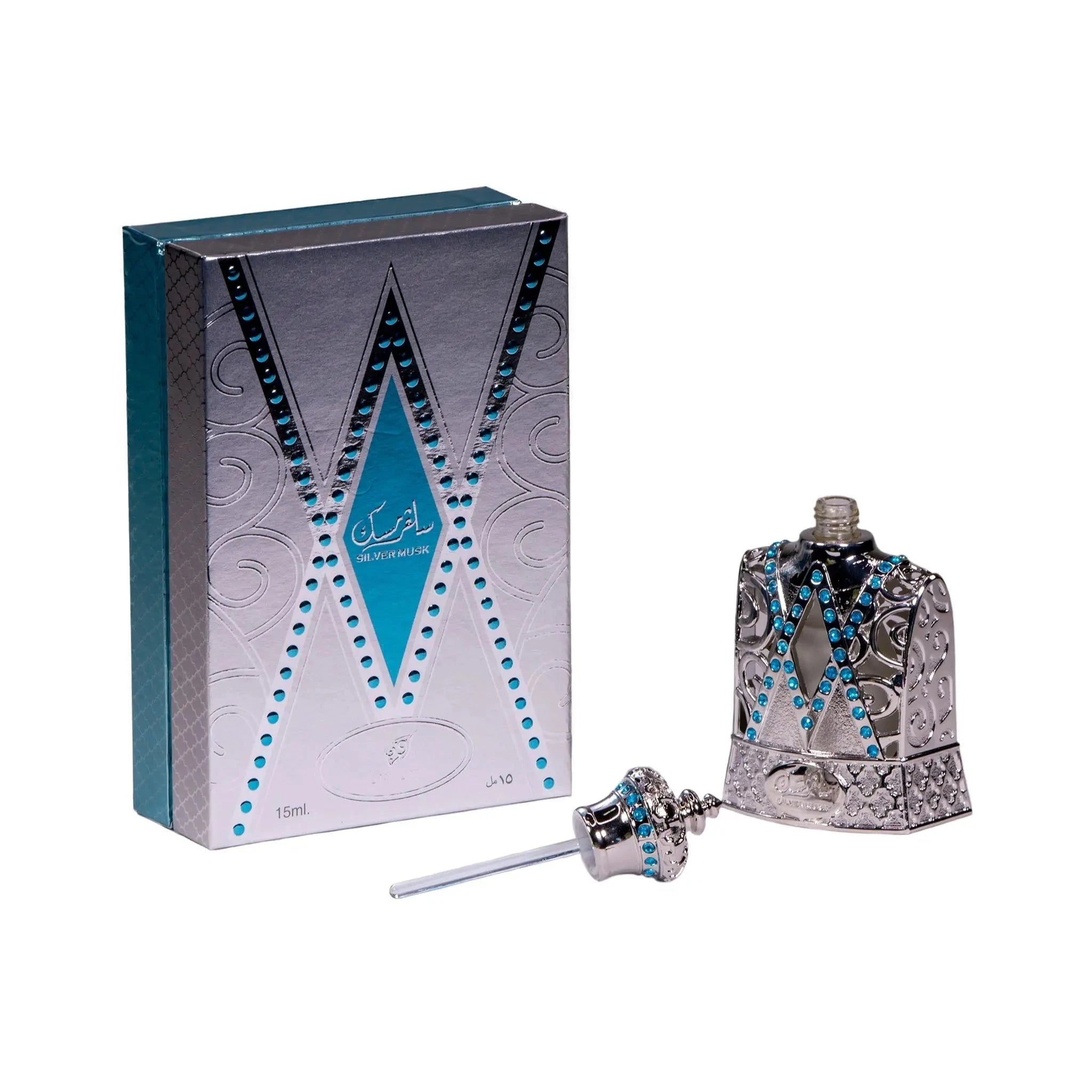 he image shows a perfume bottle with its cap removed, alongside its box packaging. The bottle and the cap are silver with detailed filigree work, and both are adorned with bright blue gemstones. The cap has a crowned design with a ring of blue gemstones at its base and a multifaceted top resembling a jewel. A silver dabber attached to the cap is visible, indicating that the perfume is applied in a traditional manner rather than sprayed. 