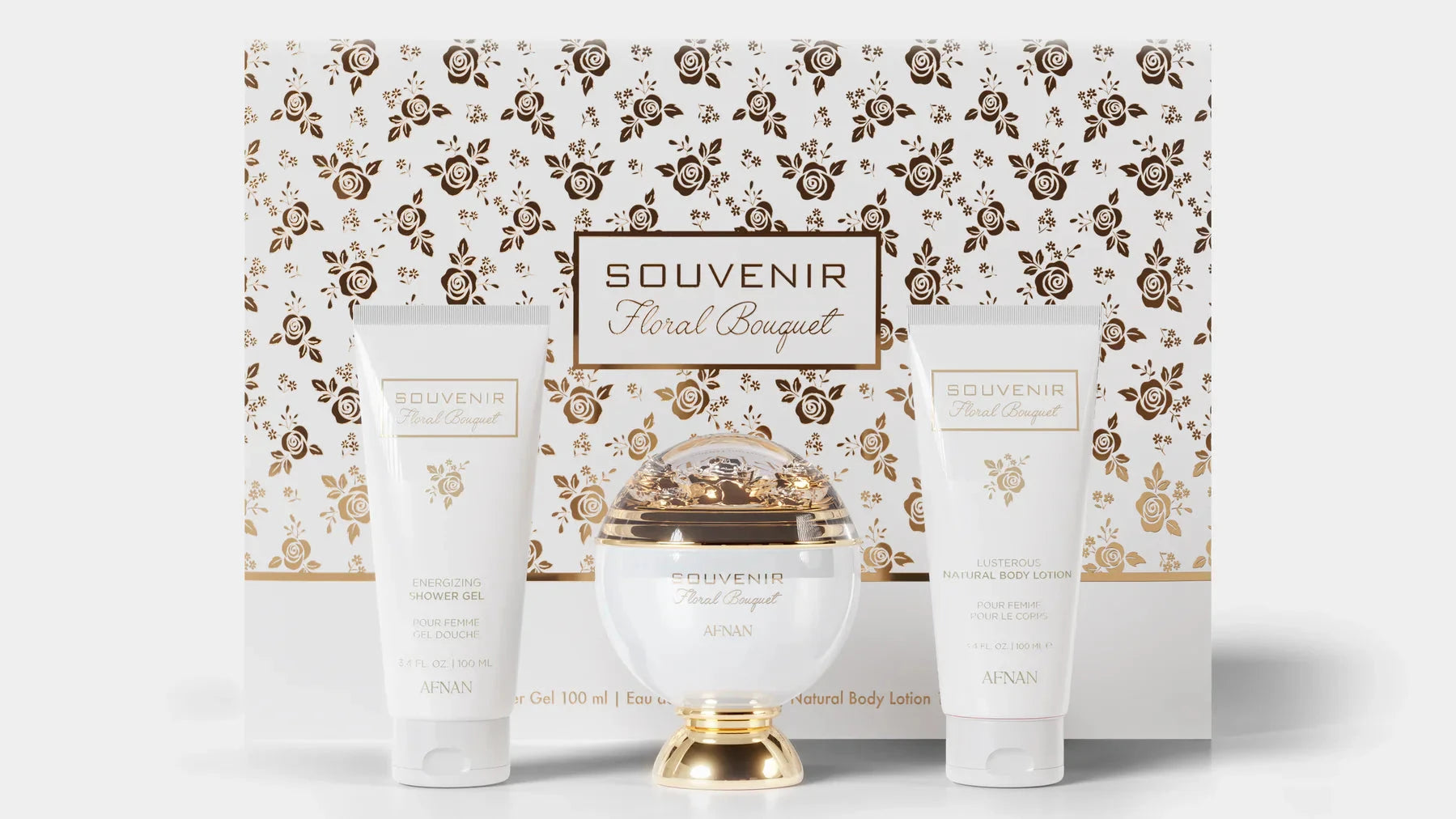 A gift set of the Souvenir Floral Bouquet by Afnan Perfumes. The packaging features an elegant floral design in gold and white. The set includes a luxurious perfume bottle with a gold and white design, an Energizing Shower Gel, and a Lusterous Natural Bod
