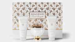 A gift set of the Souvenir Floral Bouquet by Afnan Perfumes. The packaging features an elegant floral design in gold and white. The set includes a luxurious perfume bottle with a gold and white design, an Energizing Shower Gel, and a Lusterous Natural Bod