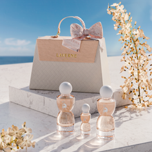 Laverne Sense Forever perfume trio set before a beige gift bag, styled with white blossoms under a clear blue sky.