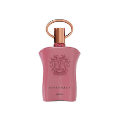 The image shows a pink perfume bottle with a metallic gold cap and a ring-shaped detail on top. The front of the bottle displays embossed text and a decorative emblem featuring the initials 'AP' in a stylized design, surrounded by a wreath-like motif. Below the emblem, the words "SUPREMACY GALA AFNAN" are printed in a simple, elegant font. The bottle has a smooth, matte finish, and there are small, pink gemstone-like embellishments around the neck.