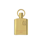The image shows a bottle of "Supremacy" eau de parfum by Afnan Perfumes. The bottle is sleek and made of reflective gold metal, giving it a luxurious and elegant appearance. The design features a circular ring attached to the top, which serves as the cap. The front of the bottle is adorned with a raised emblem featuring intricate details, positioned near the top right corner.