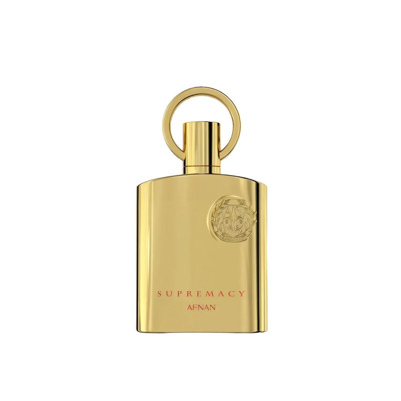 The image shows a bottle of "Supremacy" eau de parfum by Afnan Perfumes. The bottle is sleek and made of reflective gold metal, giving it a luxurious and elegant appearance. The design features a circular ring attached to the top, which serves as the cap. The front of the bottle is adorned with a raised emblem featuring intricate details, positioned near the top right corner.