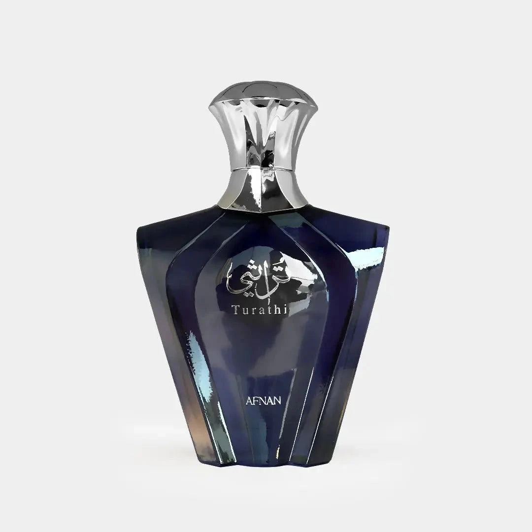 The image presents a sleek perfume bottle with a geometric design. The bottle has a deep blue color with a glossy, reflective surface, and features silver accents. The cap is silver and has an inverted cup shape that complements the bottle's shoulders. On the front, in silver lettering, is the name "Turathi" beneath an emblem with Arabic calligraphy, indicating the fragrance name or brand.