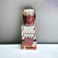 The image shows a product named "Washwashah Hand and Body Lotion." The lotion comes in a dark red container with a clear lid and is placed on top of a matching red and beige box adorned with intricate floral patterns and Arabic calligraphy. The box prominently features the product name "Washwashah" along with an illustration of a rose. The elegant and artistic packaging suggests a luxurious and high-quality skincare product.