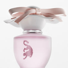 A frosted light pink perfume bottle with a matching pink leopard emblem on the front, topped with a white cap and a large pale pink satin bow, shown on a clean white background.